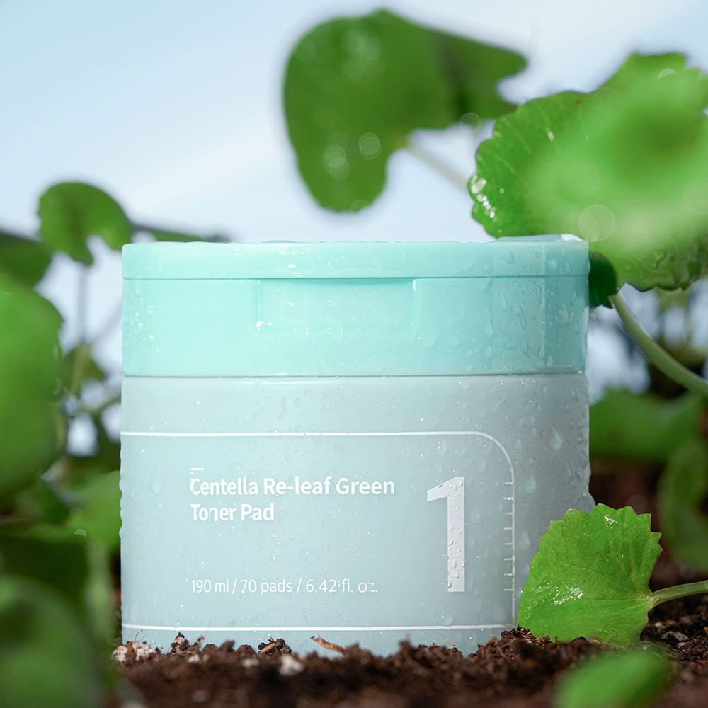 Turquoise pot met wit etiket en opschrift: Centella Re-leaf Green Toner Pad, 1. Water op de pot. Groene bladeren en aarde.