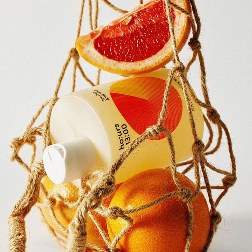 Een fles douchegel in een netzakje met sinaasappels en grapefruit. Tekst en een oranje ontwerp zijn zichtbaar op de fles.