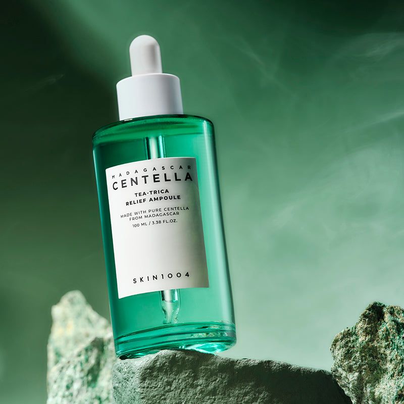 Flacon en verre vert avec bouchon et pipette blancs sur des pierres. Étiquette avec nom et informations. SKIN1004.