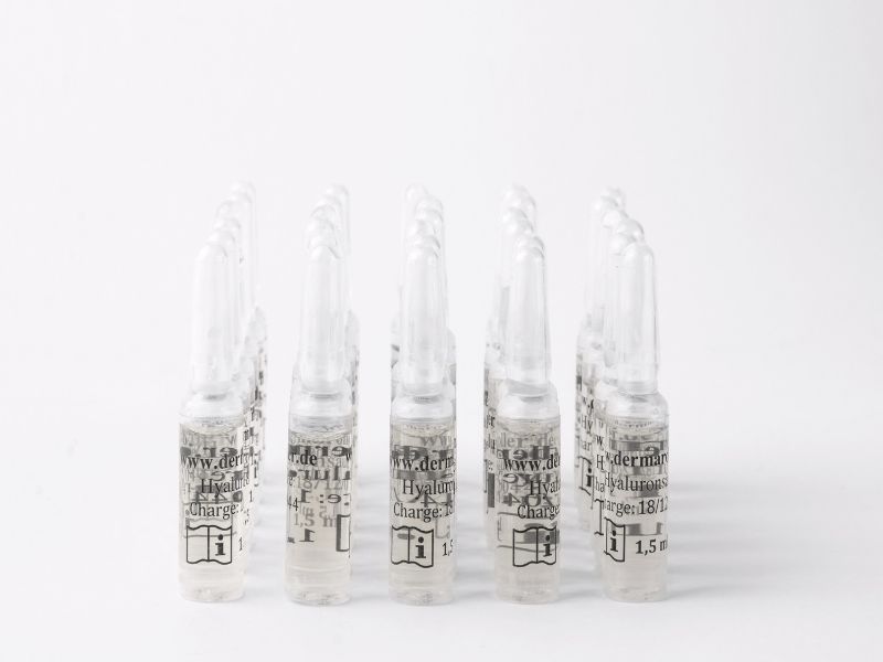 Plusieurs ampoules en verre de sérum à l'acide hyaluronique, bouchon blanc, étiquetage blanc.