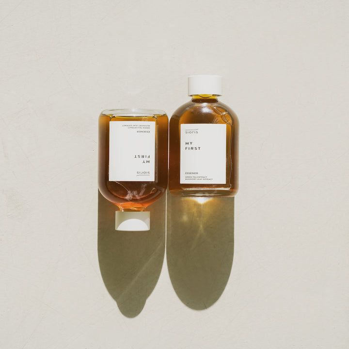 Deux flacons en verre avec bouchon blanc et étiquette. Texte: MY FIRST ESSENER. Les deux flacons projettent des ombres.