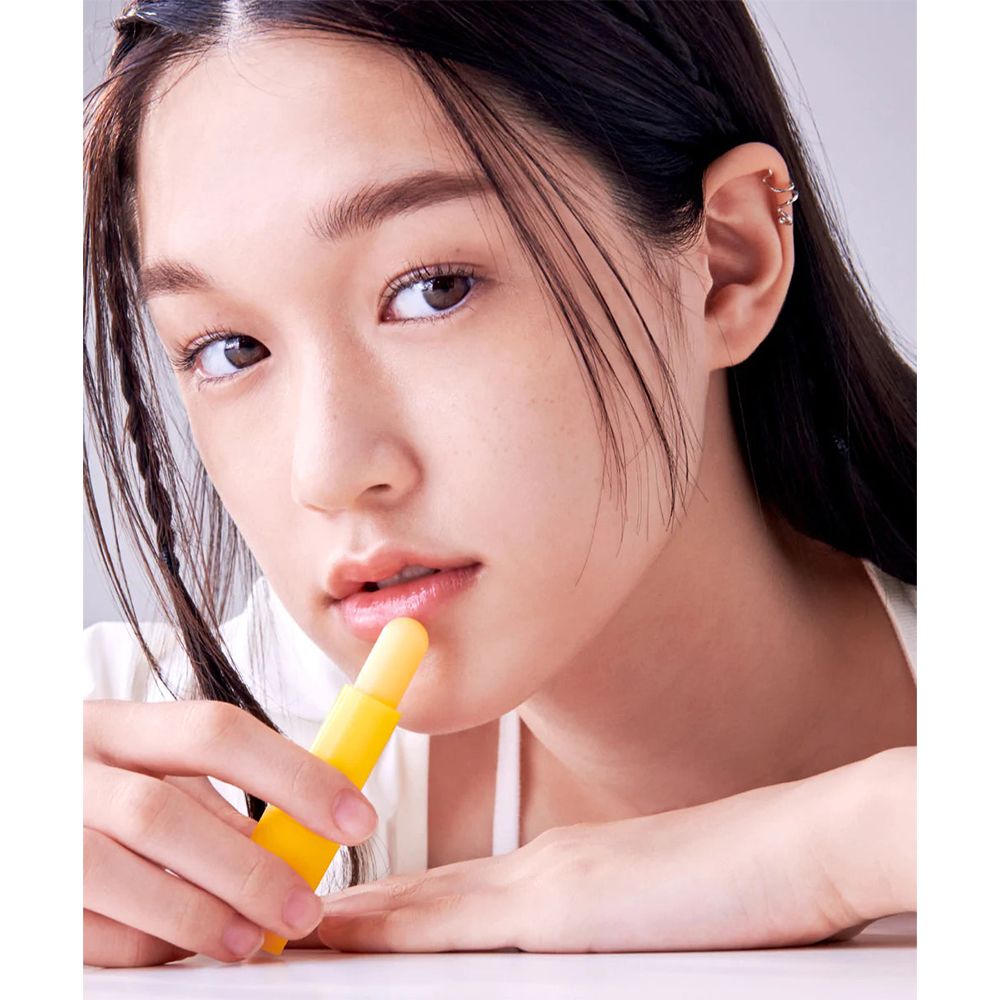 Jonge vrouw houdt een gele lippenbalsem-stick tegen haar lippen. Close-up, lichte achtergrond.