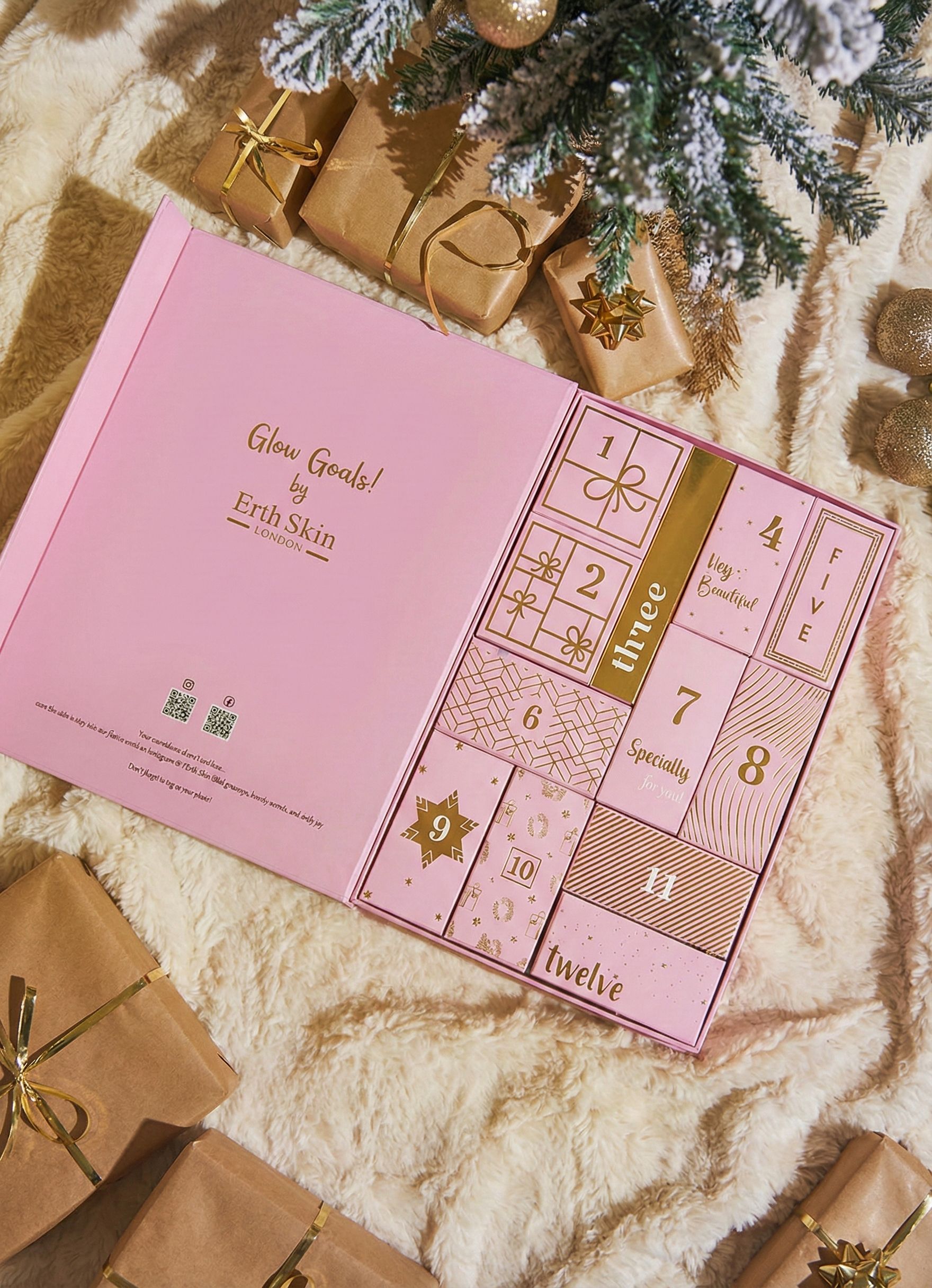 Open roze adventskalenderdoos met 12 deurtjes, omringd door cadeaupakketten en dennentakken.