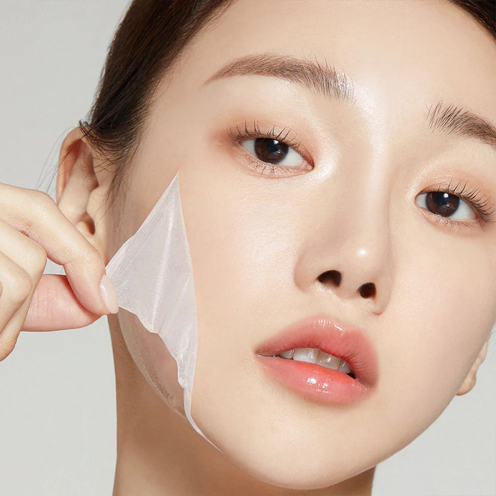 Une femme retire le 'Collagen Night Wrapping Mask' séché de son visage.