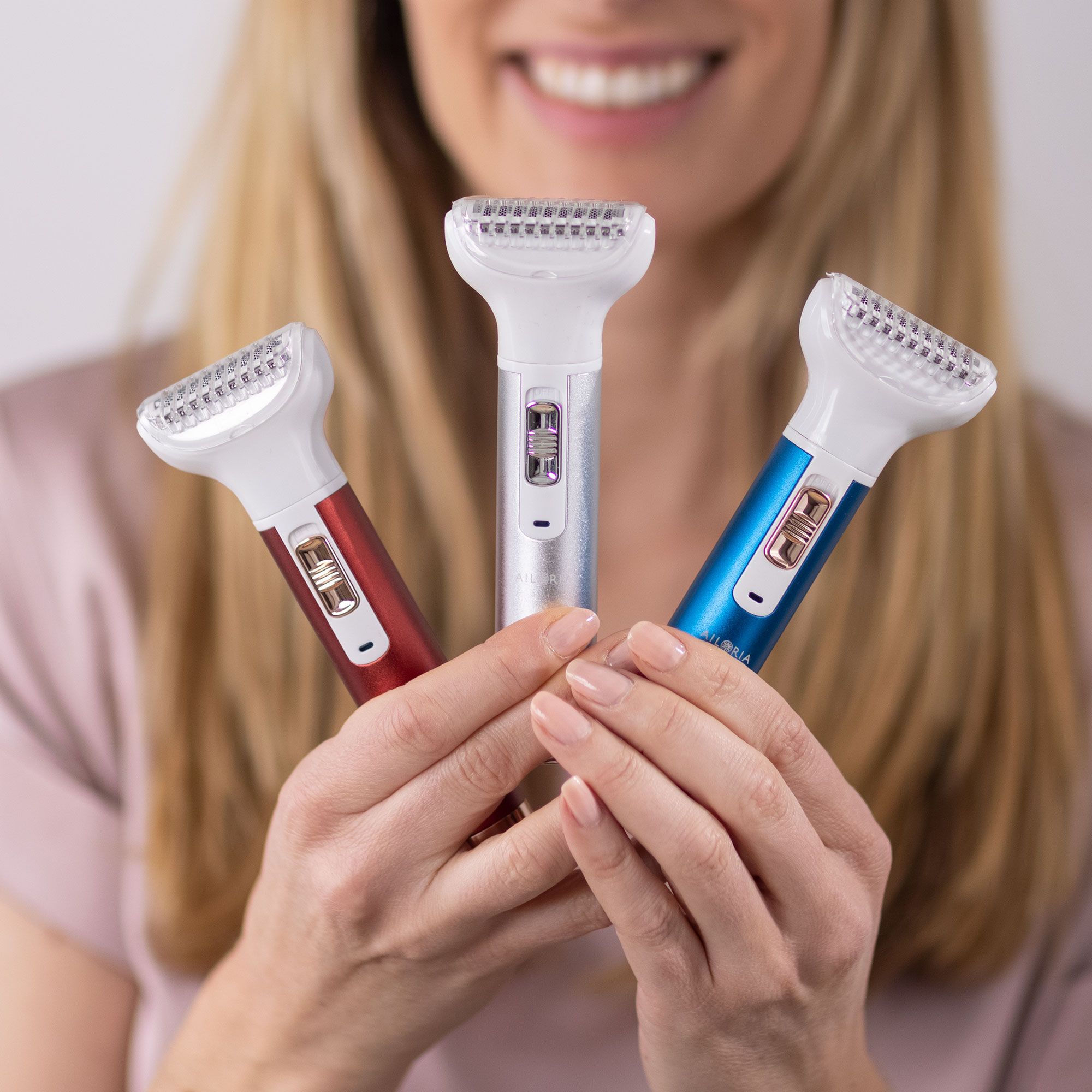 Trois rasoirs avec tête blanche et manches colorées. Femme les tient. Rouge, argent et bleu. Logo AILORIA non visible.