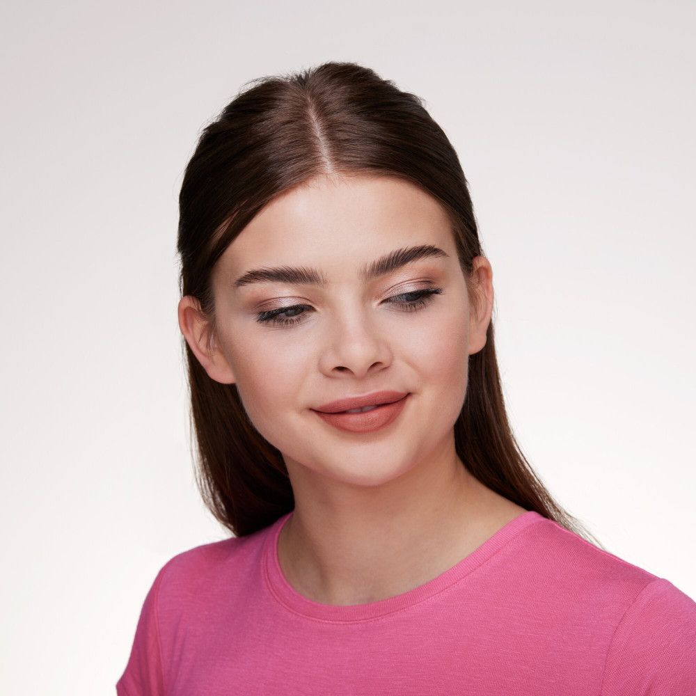 Portret van een jonge vrouw met een roze top en subtiele make-up, inclusief oogschaduw.