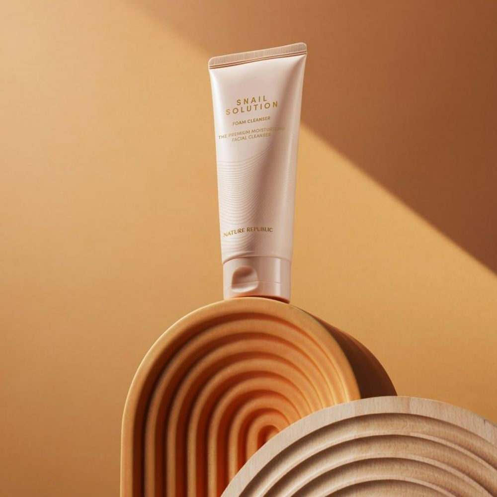 Tube beige sur structure en bois. Texte du produit: Snail Solution Foam Cleanser.