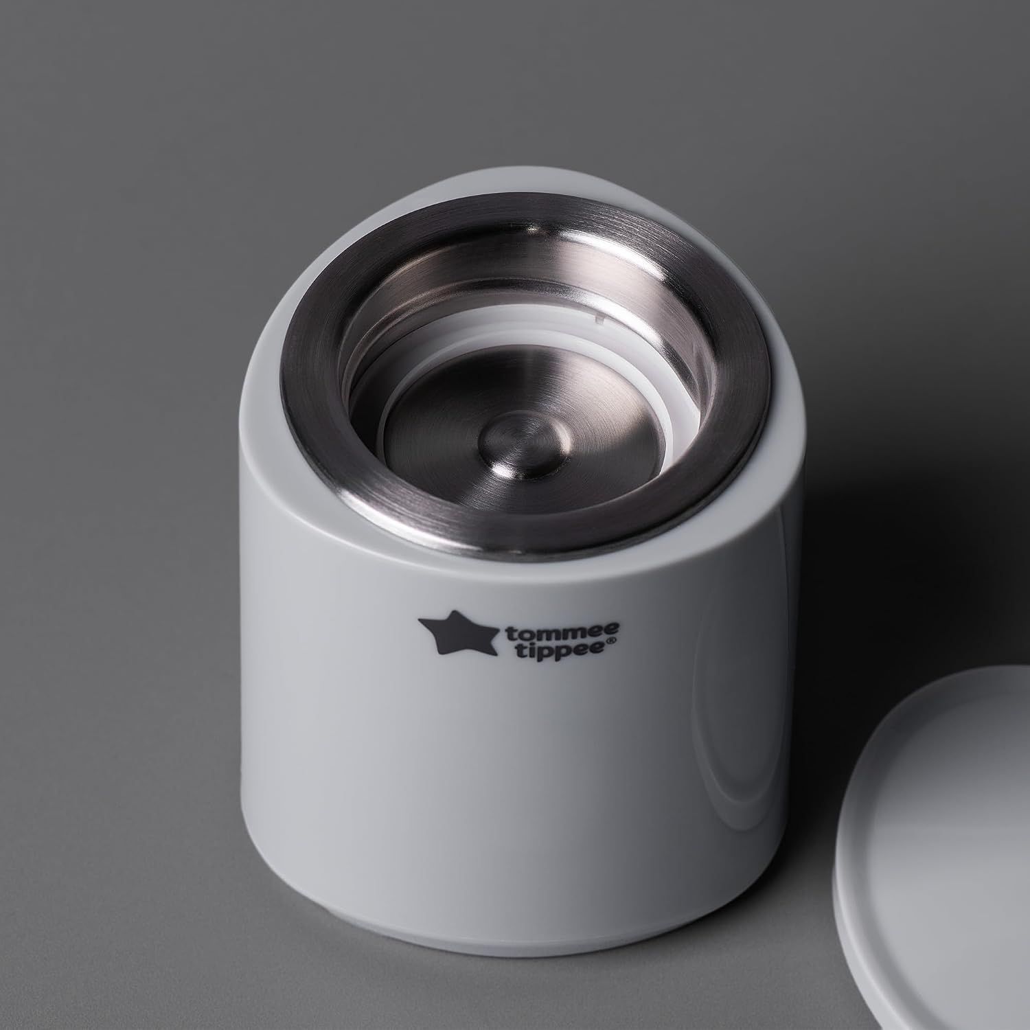 Un chauffe-biberon blanc avec un anneau supérieur argenté et le logo Tommee Tippee.
