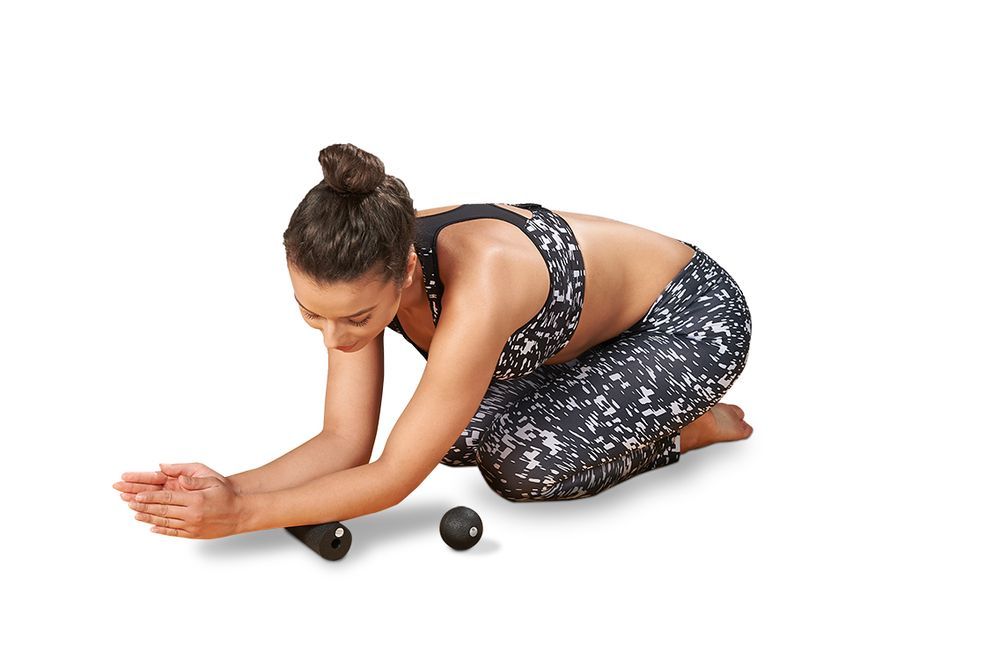 Femme en tenue de sport, à genoux, avec rouleau de fascia et petite balle. Sur fond blanc.
