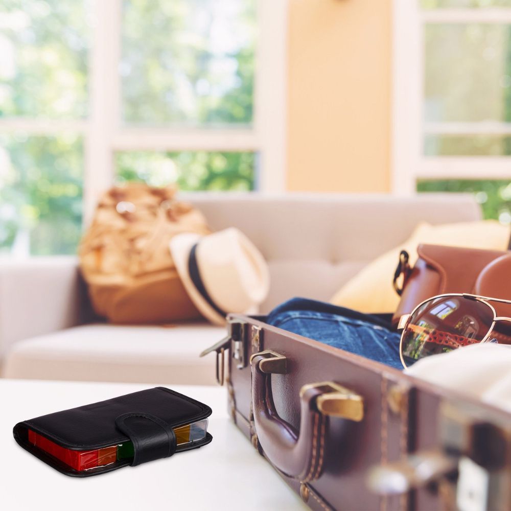 Zwarte pillendoos op tafel, naast koffer. Etui gesloten, met riemgesp.