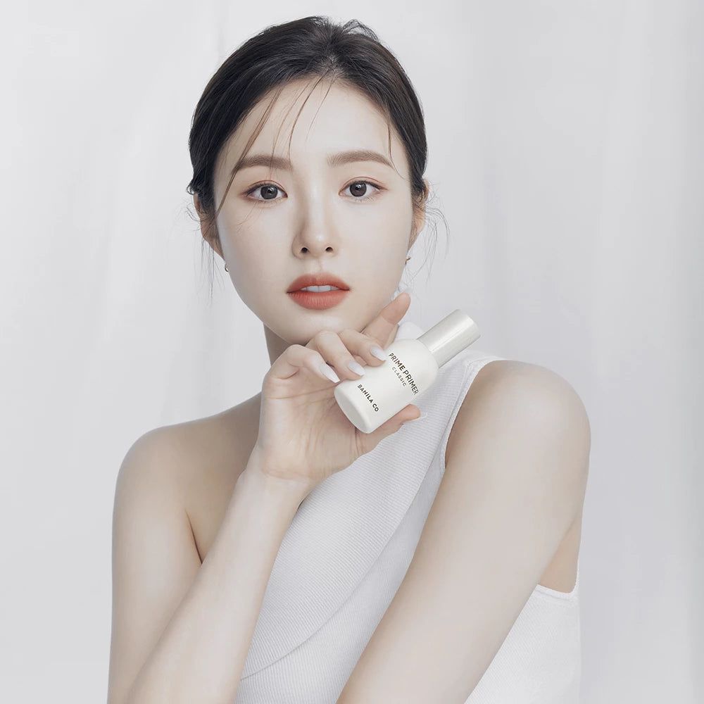 Femme tenant une bouteille blanche. Inscription : PRIME PRIMER CLASSIC, BANILA CO. La femme porte un haut blanc.