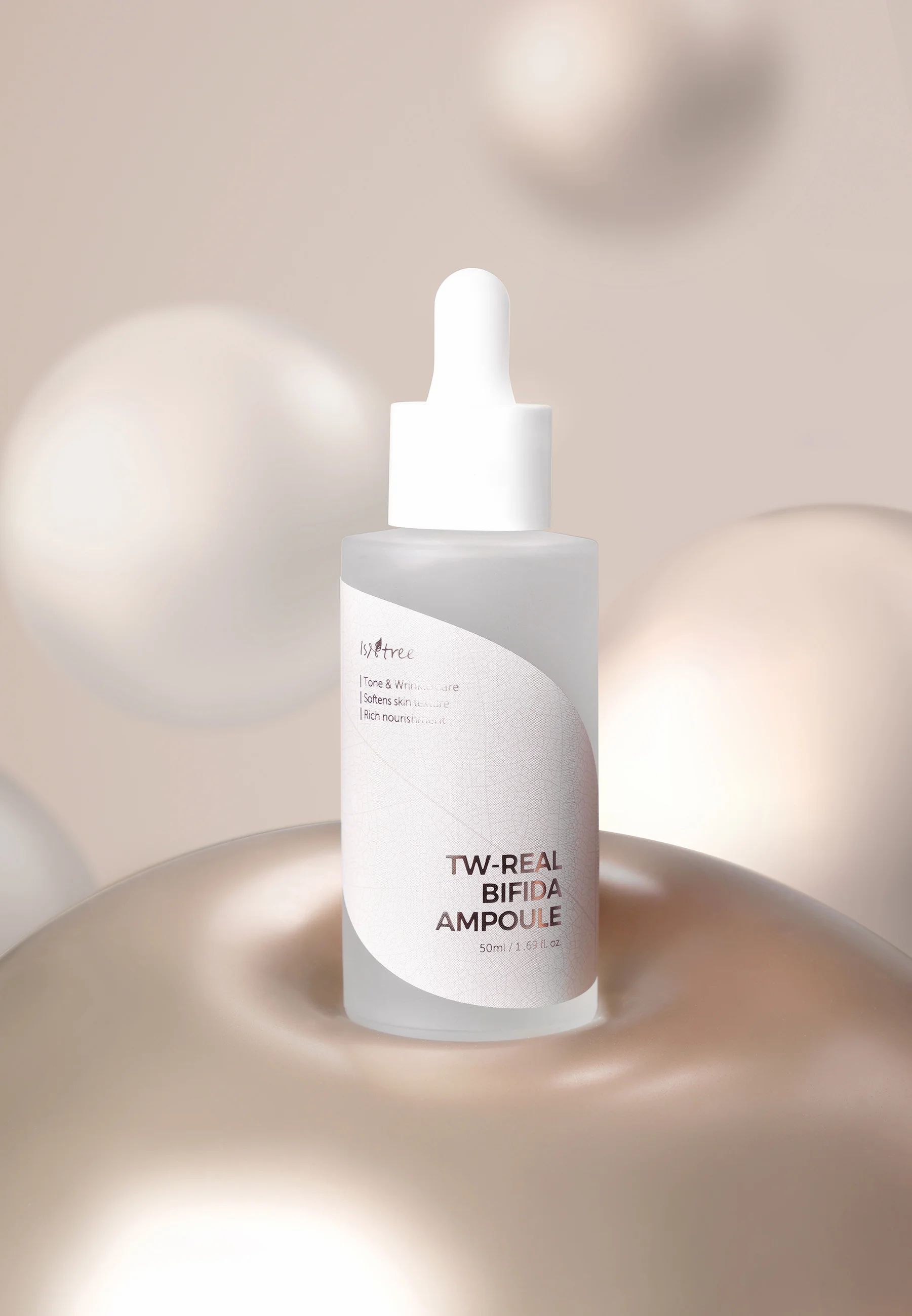 Transparante fles met witte dop en opschrift TW-REAL BIFIDA AMPOULE. Op gouden oppervlak, achtergrond met bollen.