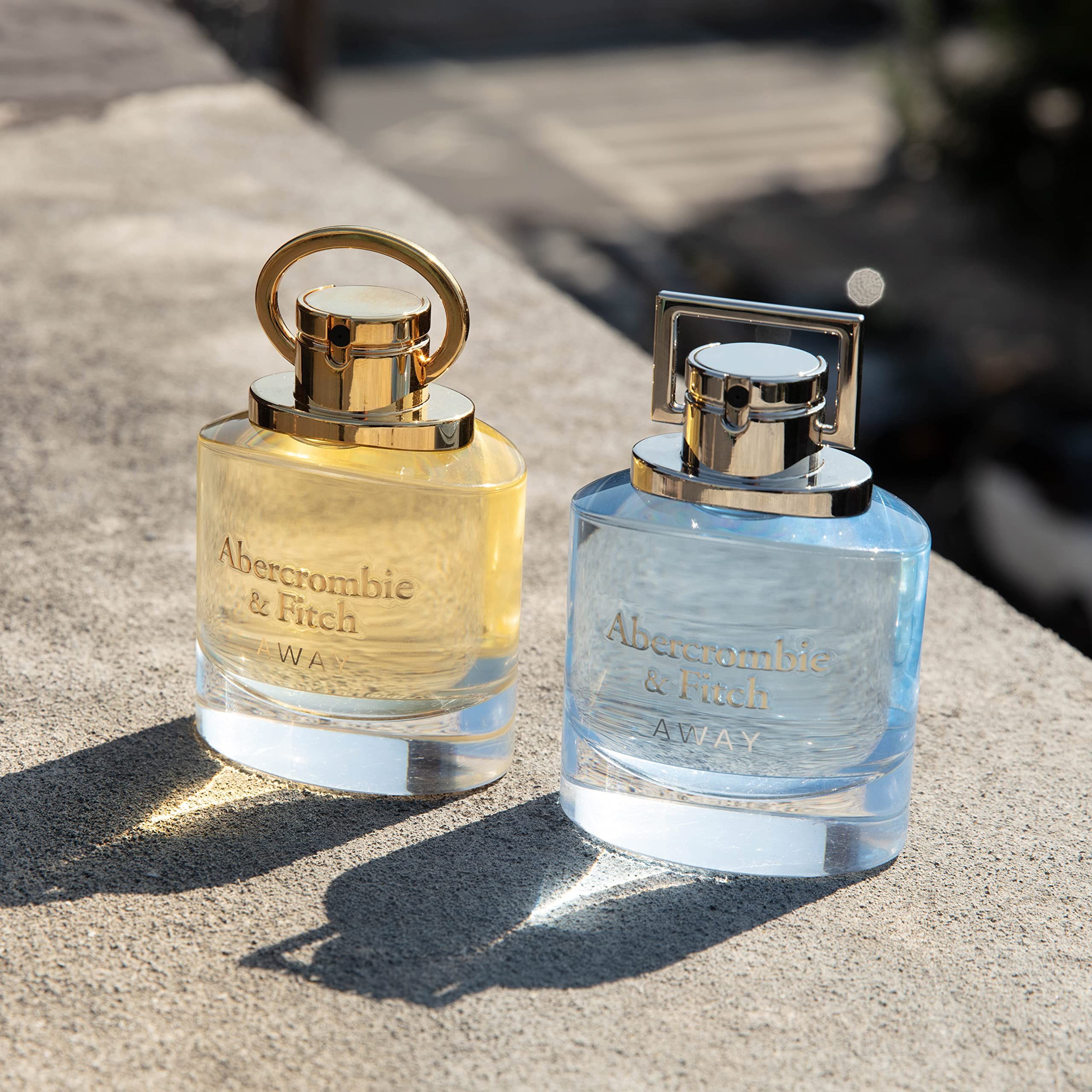 Deux flacons d'Eau de Toilette. Un jaune, un bleu. Inscription : Abercrombie & Fitch AWAY. Posés sur un mur en pierre.