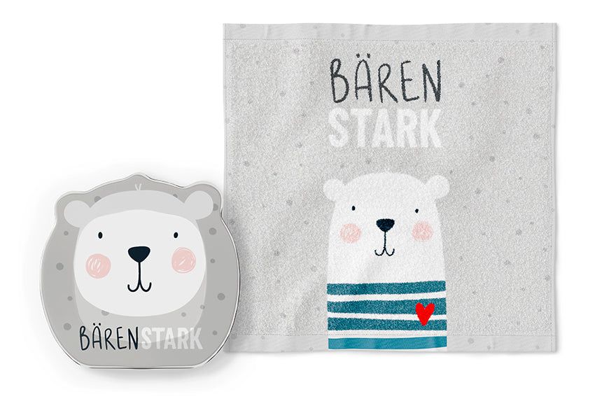Grijze handdoek met berenillustratie en opschrift « Bären Stark ». Daarnaast een berenplateau.