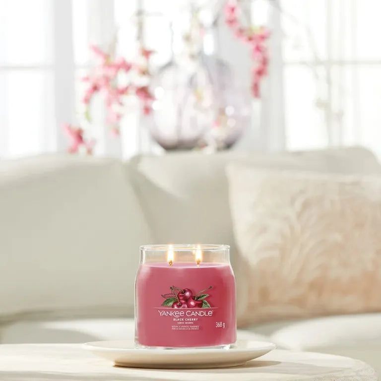 Bougie parfumée rouge sur assiette. Étiquette cerise, deux mèches. Sur table devant canapé. Yankee Candle.