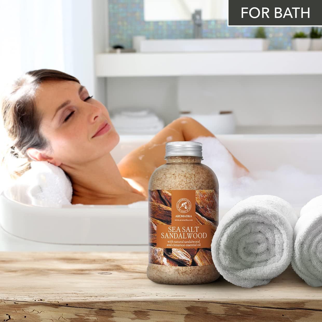 Femme savourant un bain moussant, avec sel de bain AROMATIKA bois de santal et serviettes à côté.