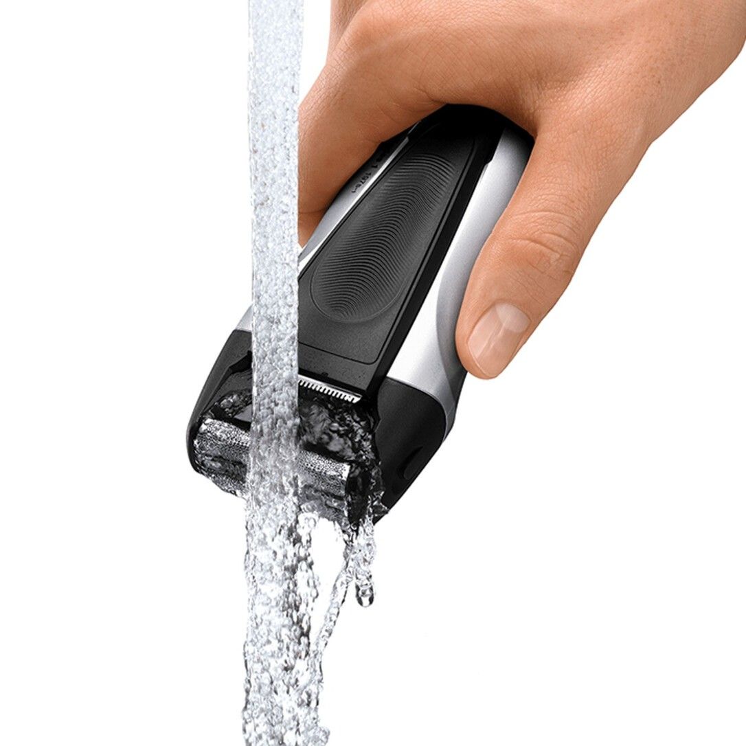 Un homme tient un rasoir électrique Braun Series 1 sous l'eau courante pour le nettoyage.