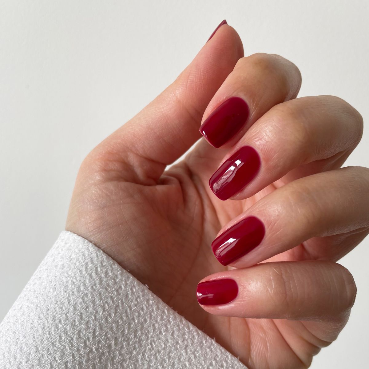 Main avec ongles vernis en rouge foncé. Les ongles sont courts et brillants. Le fond est blanc.