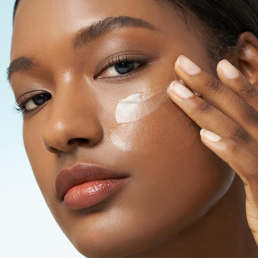 Une femme applique une crème blanche sur sa joue, gros plan.