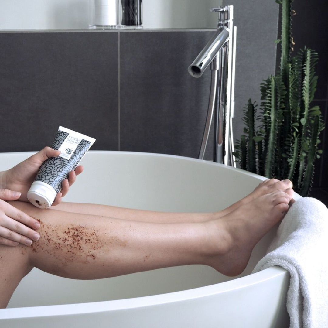 Personne dans une baignoire. Tient un tube de Body Scrub. Jambe exfoliée. Marque : Australian Bodycare. Contexte : salle de bain.