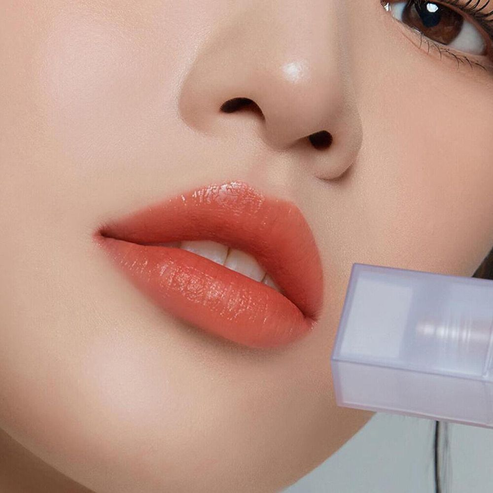 Lèvres maquillées avec un gloss abricot. Un applicateur est visible.