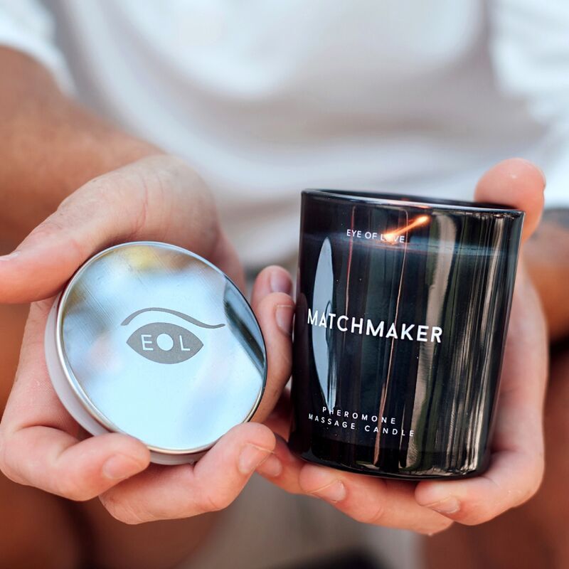 Mains tenant une bougie de massage noire 'Matchmaker' et son couvercle argenté avec logo EOL.