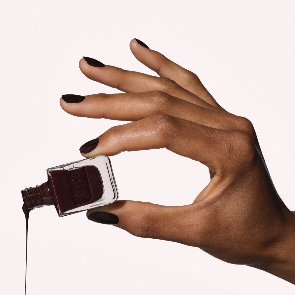 Donkerbruine nagellak druipt uit een glazen flesje, vastgehouden door een hand met bijpassende nagels.