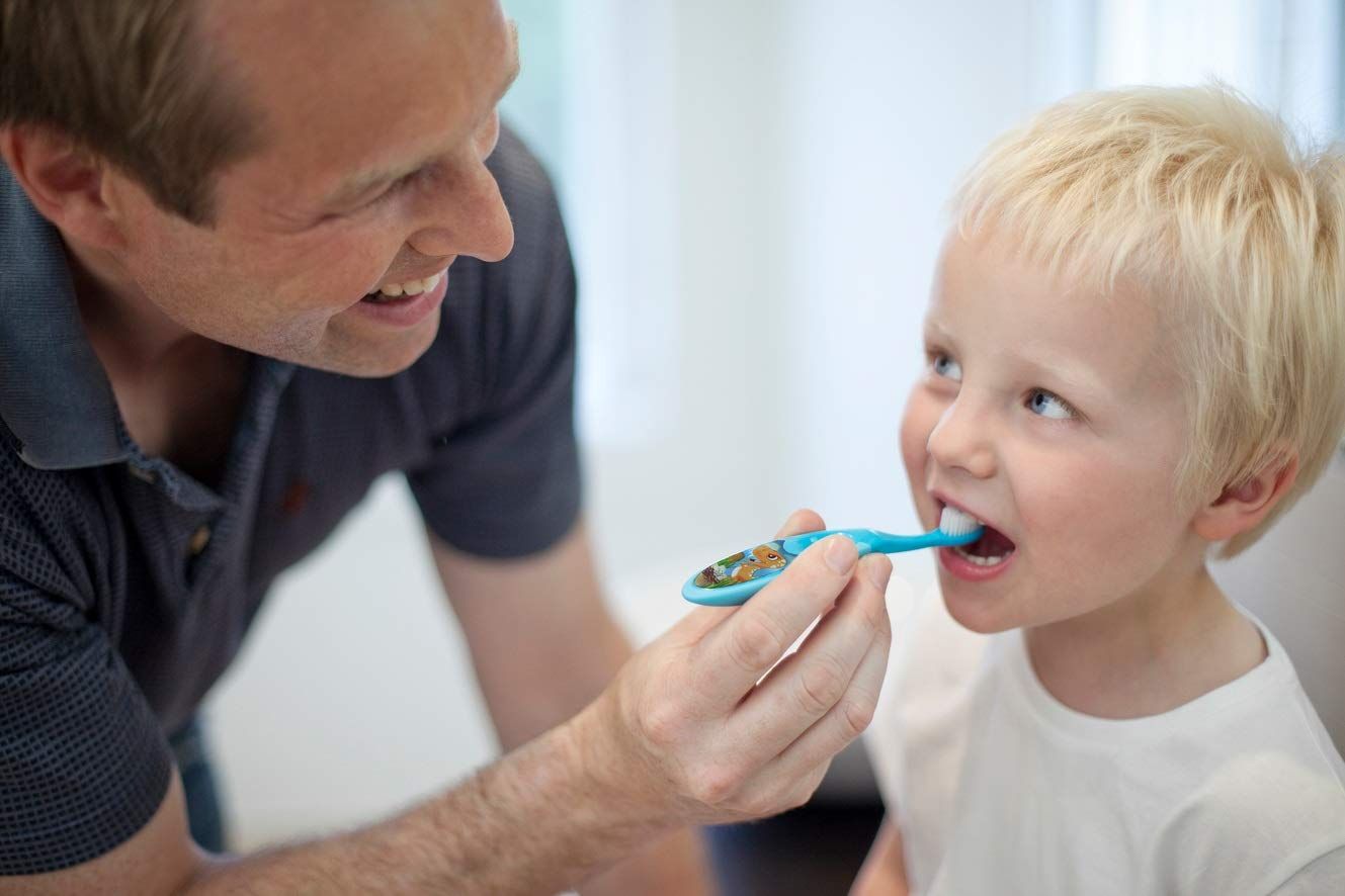 Un père aide son enfant à se brosser les dents avec une brosse à dents bleue.