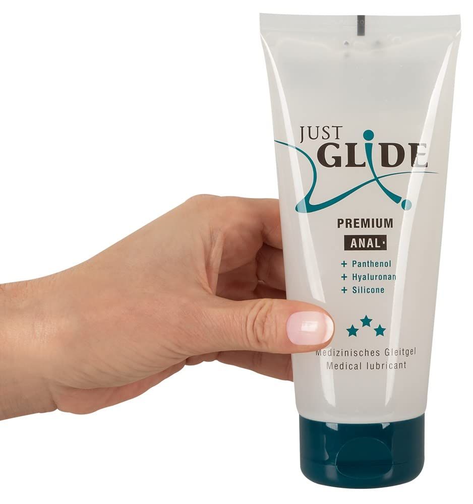 Main tenant un tube de gel lubrifiant Just Glide Premium Anal. Récipient transparent avec bouchon bleu.