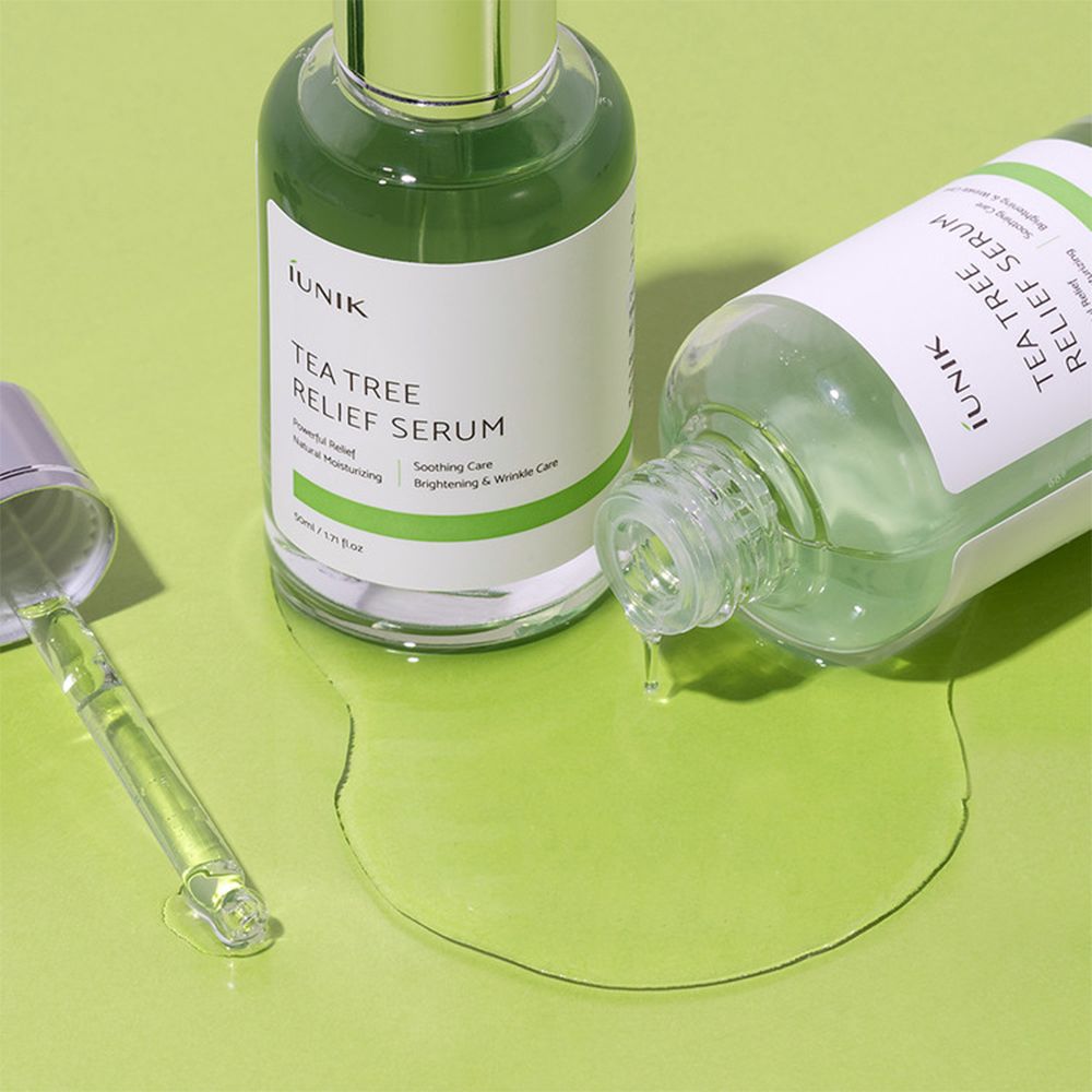 Twee iUNIK Tea Tree Relief Serum flessen, één ligt omgevallen met gemorst serum.