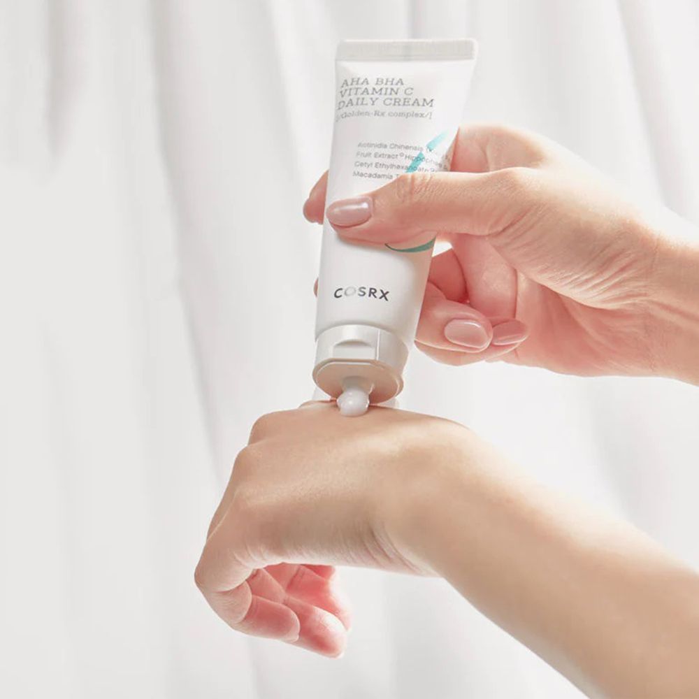 Handen houden een tube AHA BHA Vitamin C Daily Cream vast. Crème wordt op de hand gedrukt.