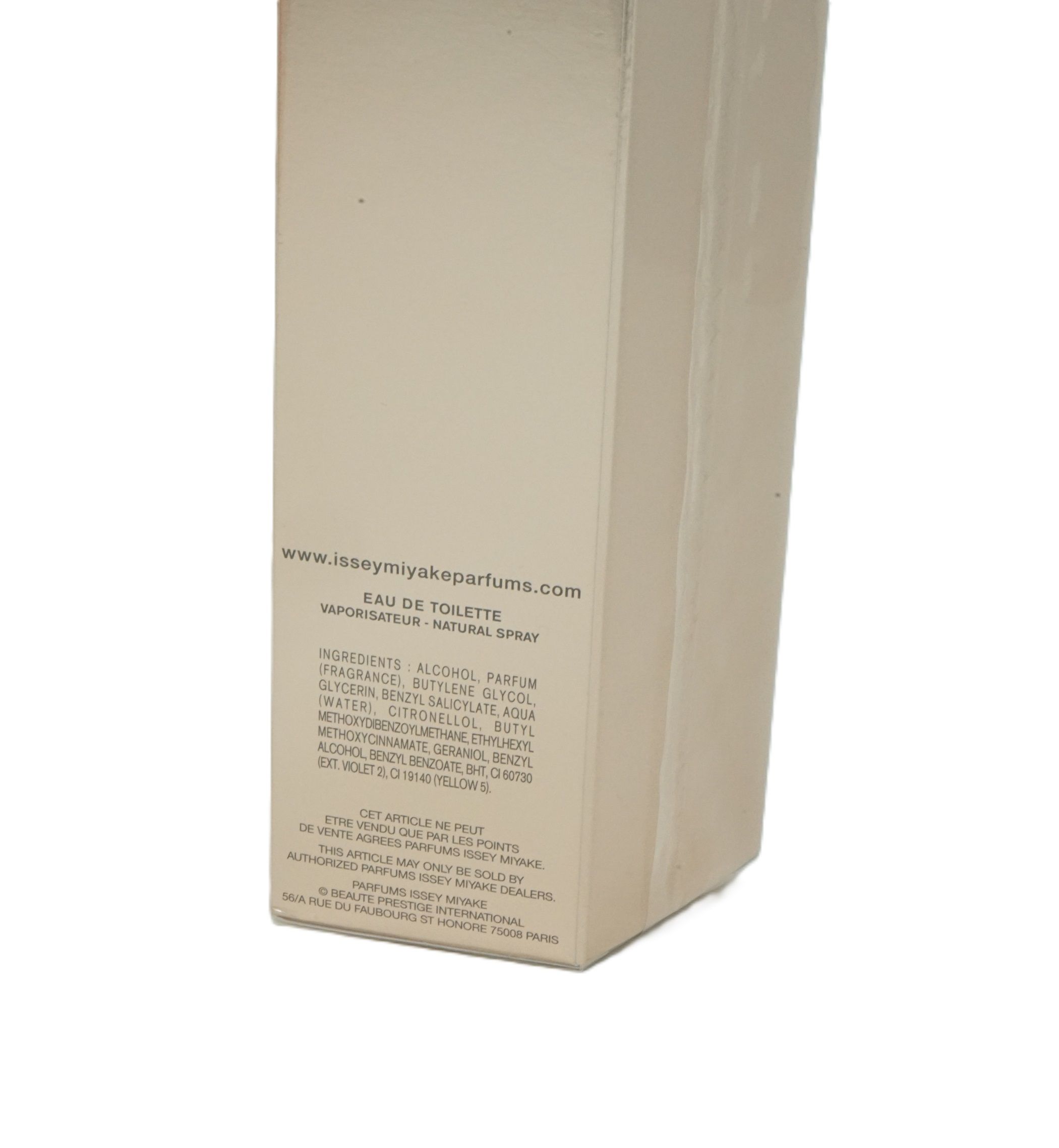 Boîte en carton beige avec texte. Contient des informations telles que les ingrédients, le site web et l'adresse du fabricant. "Eau de Toilette".