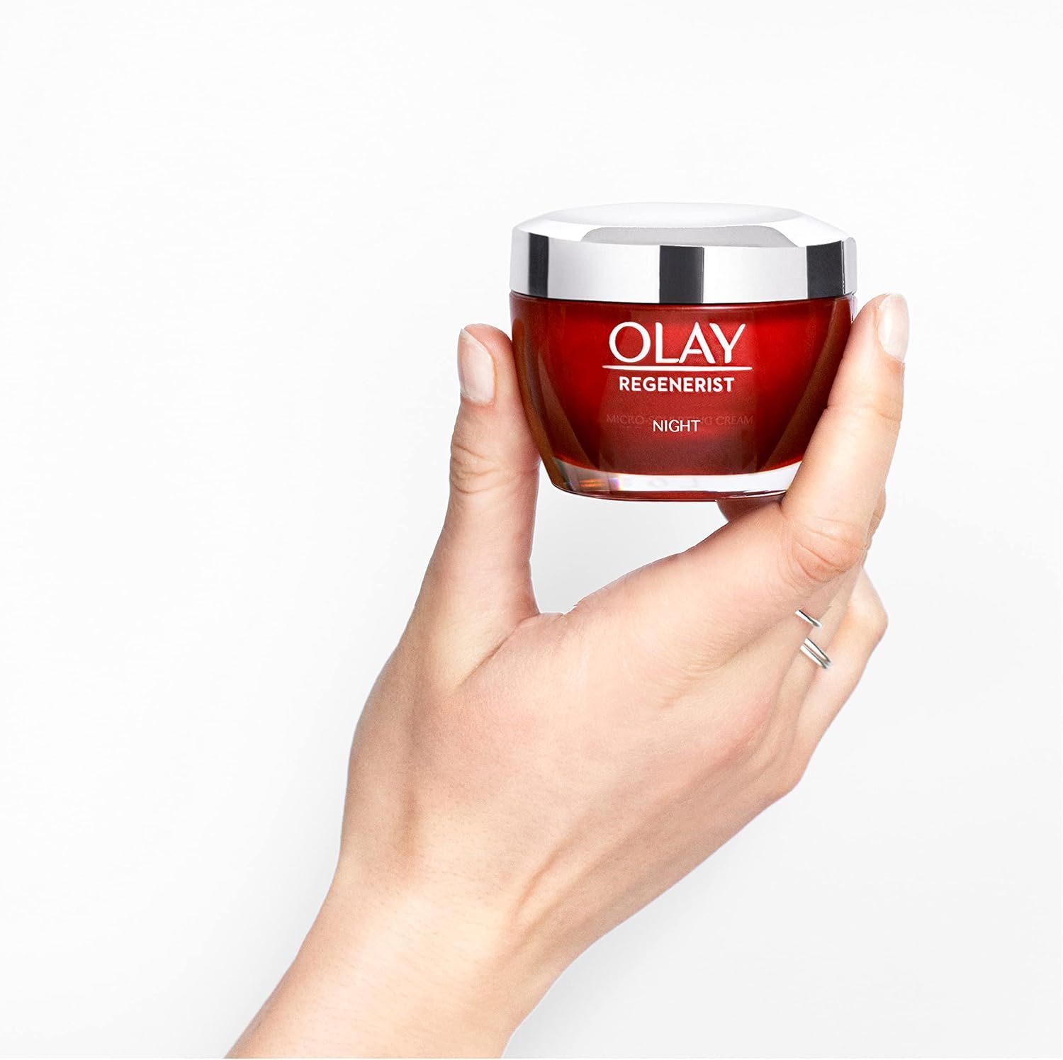 Pot de crème de nuit Olay Regenerist rouge avec couvercle argenté, tenu dans une main.