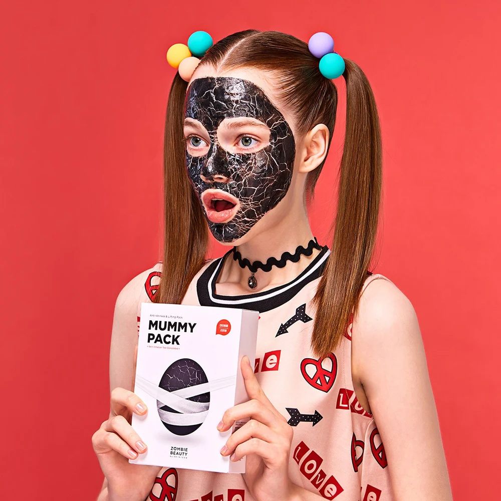 Personne avec masque facial et une boîte blanche avec l'inscription MUMMY PACK.
