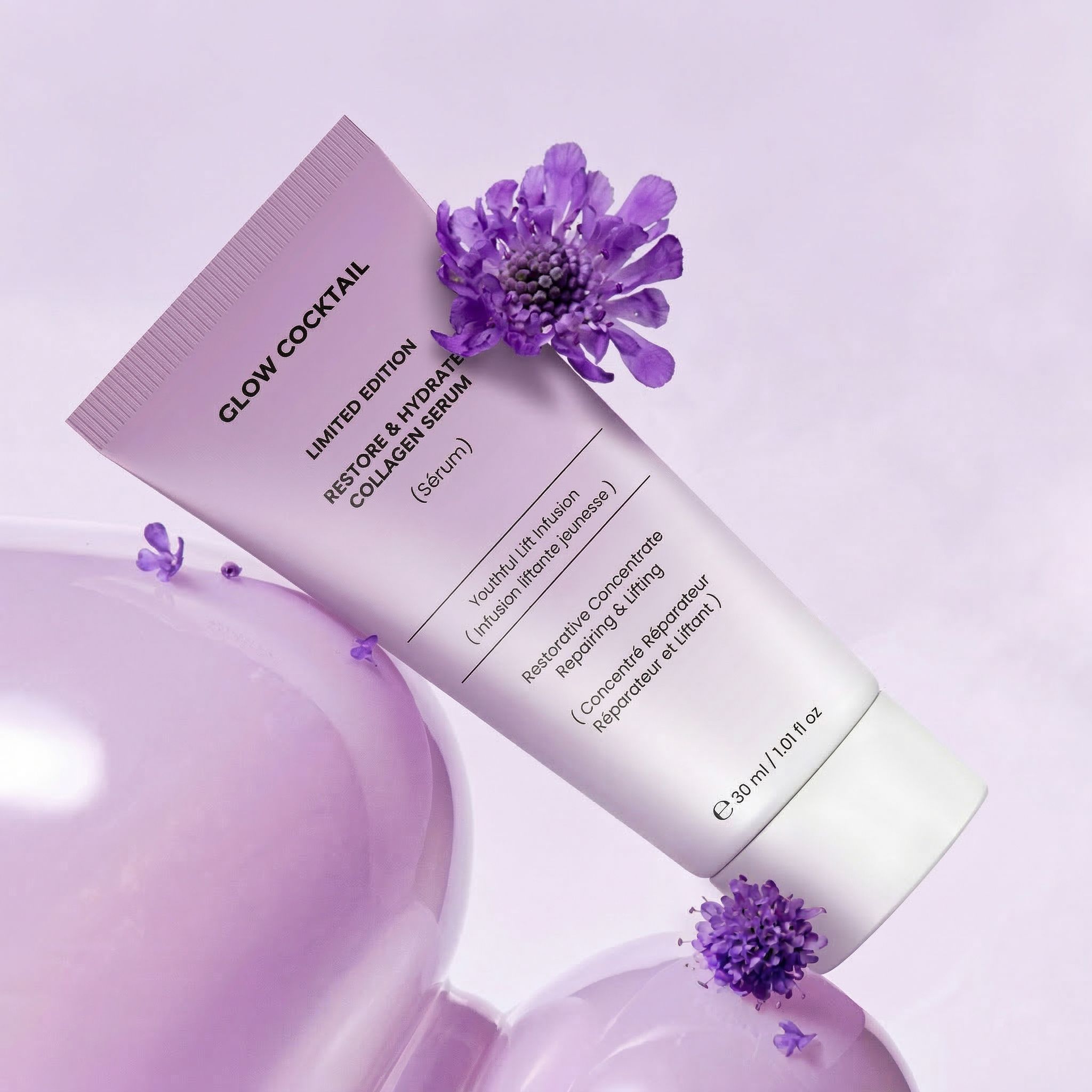 Een lichtpaarse tube met de tekst "Glow Cocktail Restore & Hydrate Collagen Serum", met paarse bloemen en bubbels.