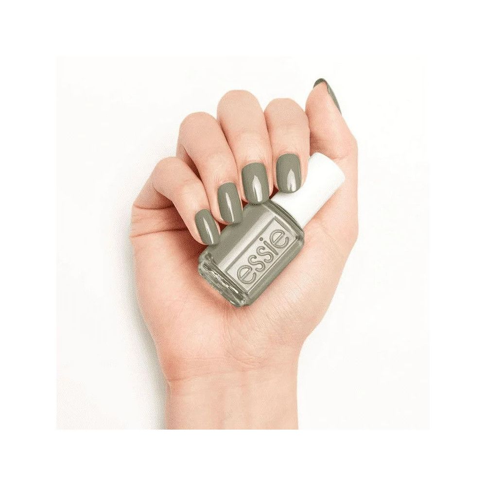 Hand met gelakte nagels en nagellakflesje. Flesje met witte dop, groen-grijze nagellak. Essie-logo zichtbaar.