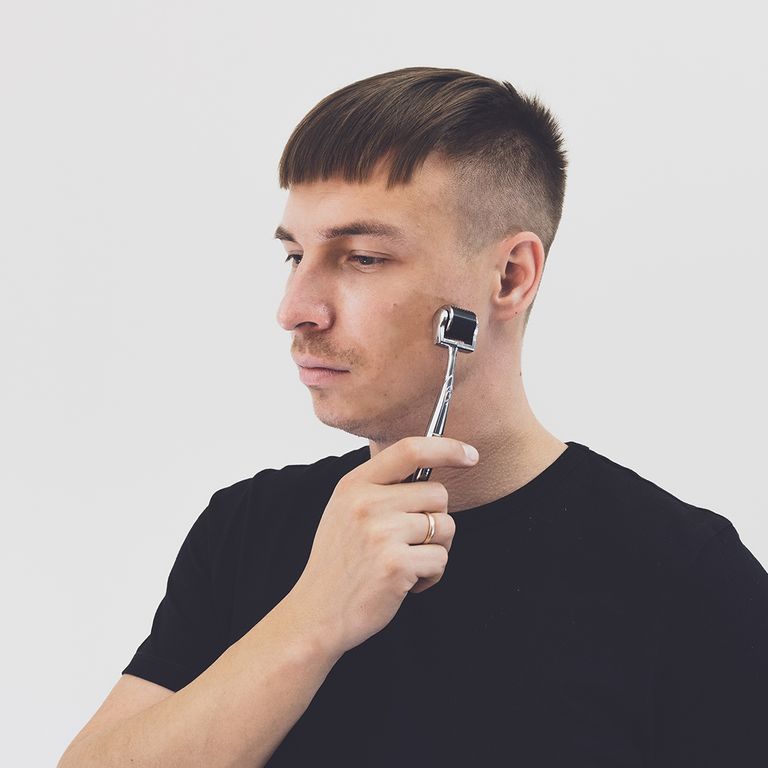 Man met kort haar gebruikt een zilverkleurige CIT Face Roller op de rechterwang.