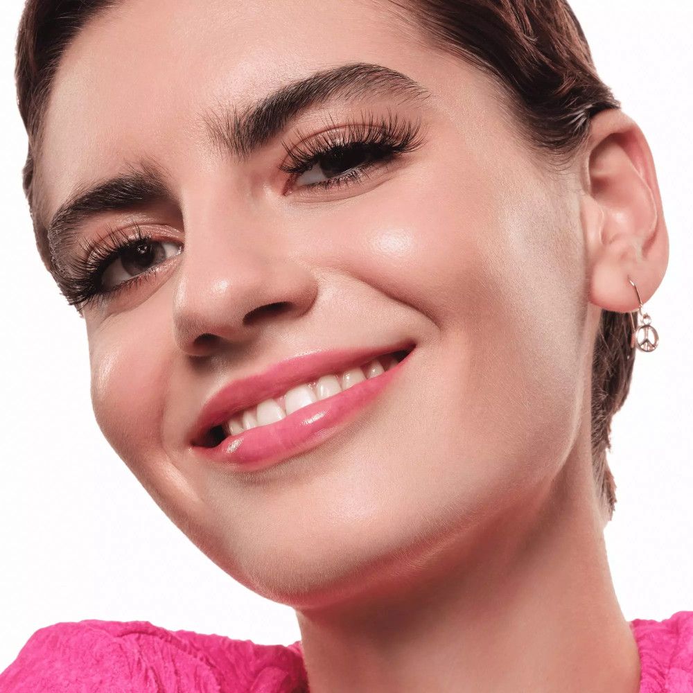 Gros plan d'une personne portant de faux cils. La personne sourit et porte des boucles d'oreilles.