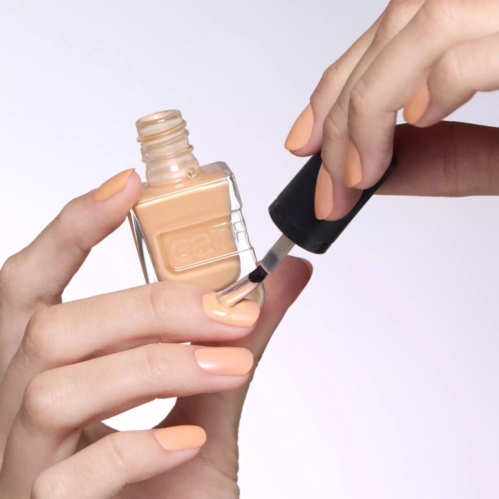 Mains vernissant les ongles avec du vernis à ongles. Vernis à ongles orange clair. Flacon avec nom de marque.