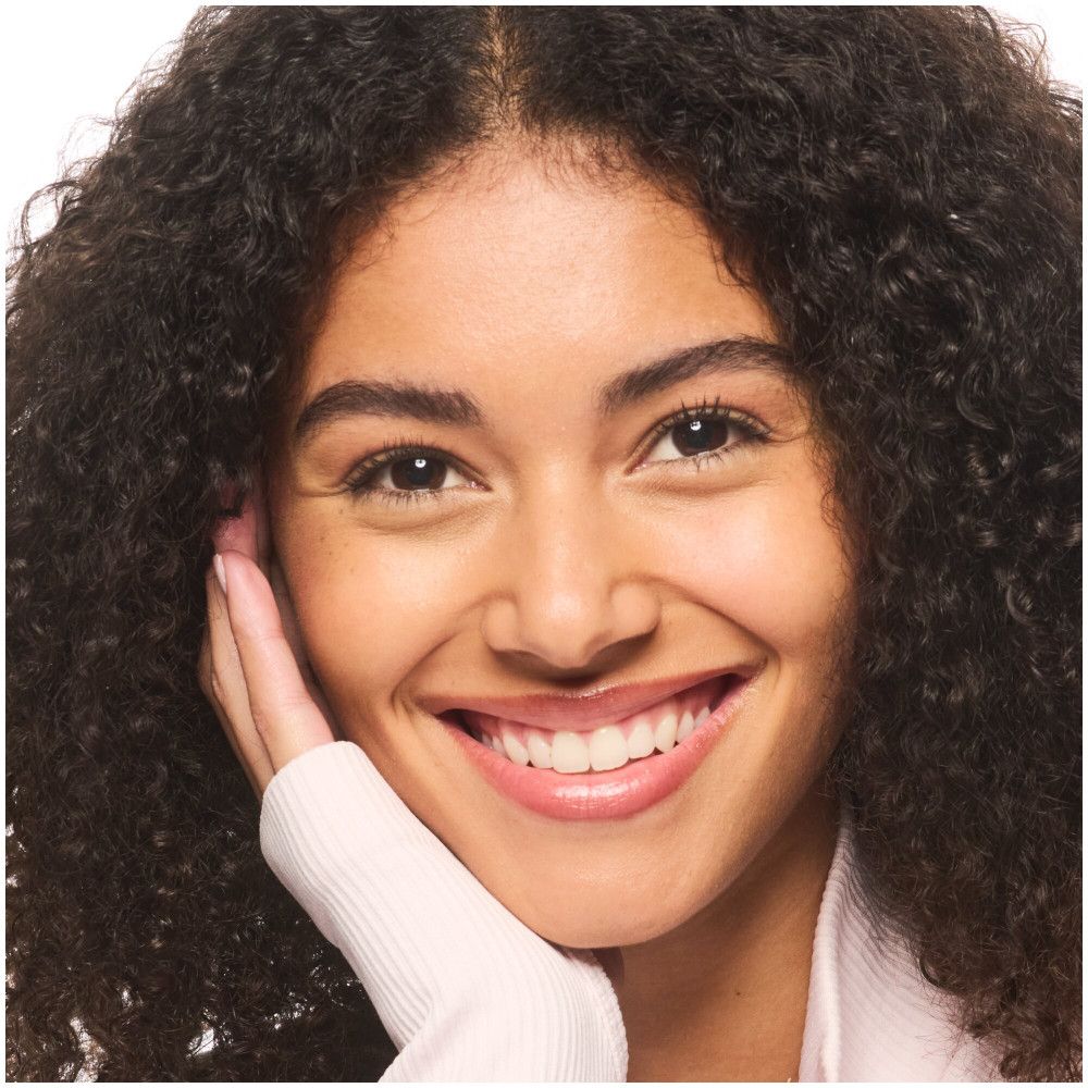 Portret van een lachende vrouw met krullend haar. Ze ondersteunt haar kin met haar hand.