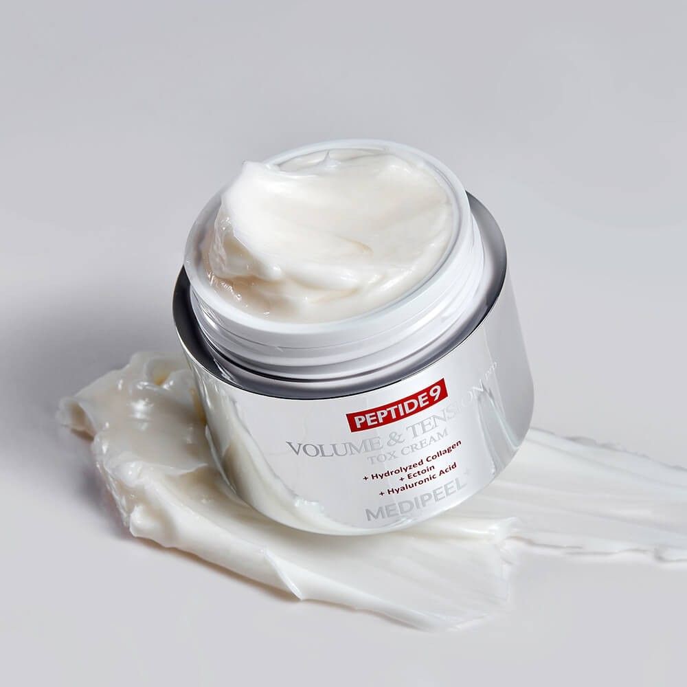 Open crème pot met zilveren body, gevuld met witte crème. Crème is uitgesmeerd op het oppervlak.