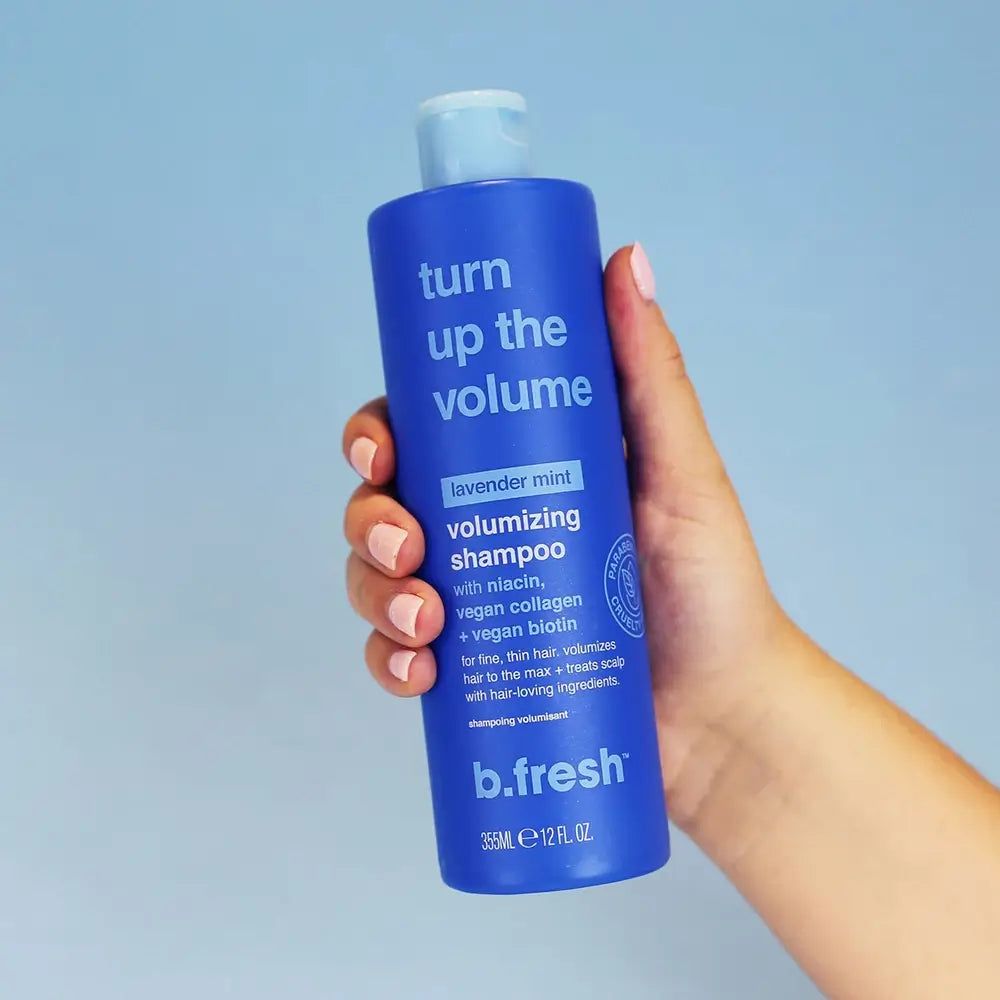 Flacon de shampooing bleu "Turn Up The Volume" de b.fresh. Contient de la niacine, du collagène végétalien et de la biotine. Tenue à la main.