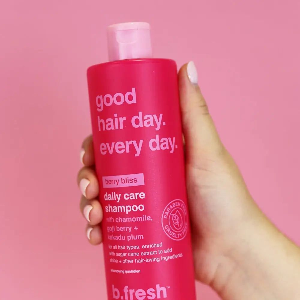 Rode shampoo fles in hand. Tekst: good hair day. every day. berry bliss daily care shampoo. b.fresh. Roze achtergrond.