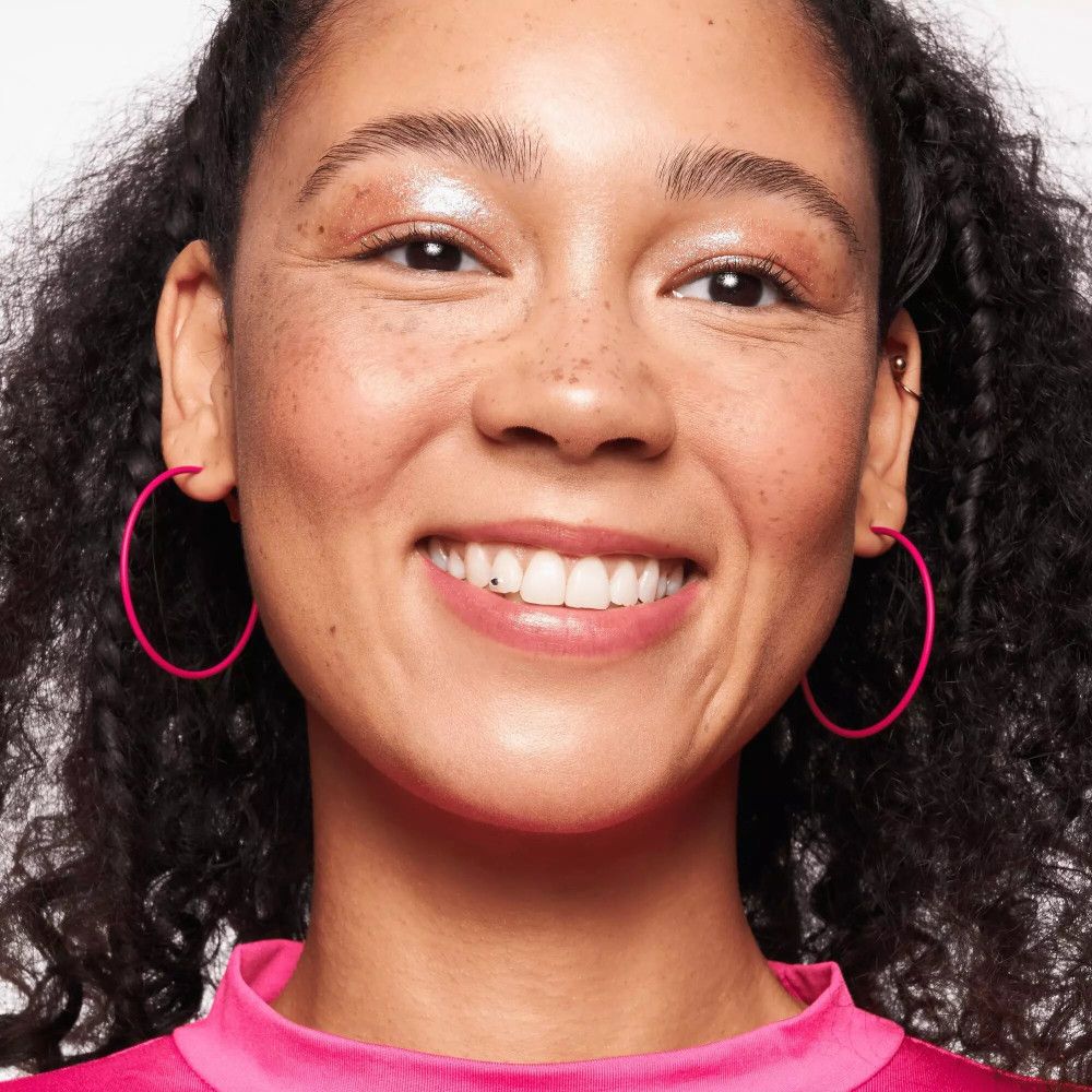 Gros plan d'une femme avec des boucles d'oreilles roses. Elle a des taches de rousseur et est maquillée.