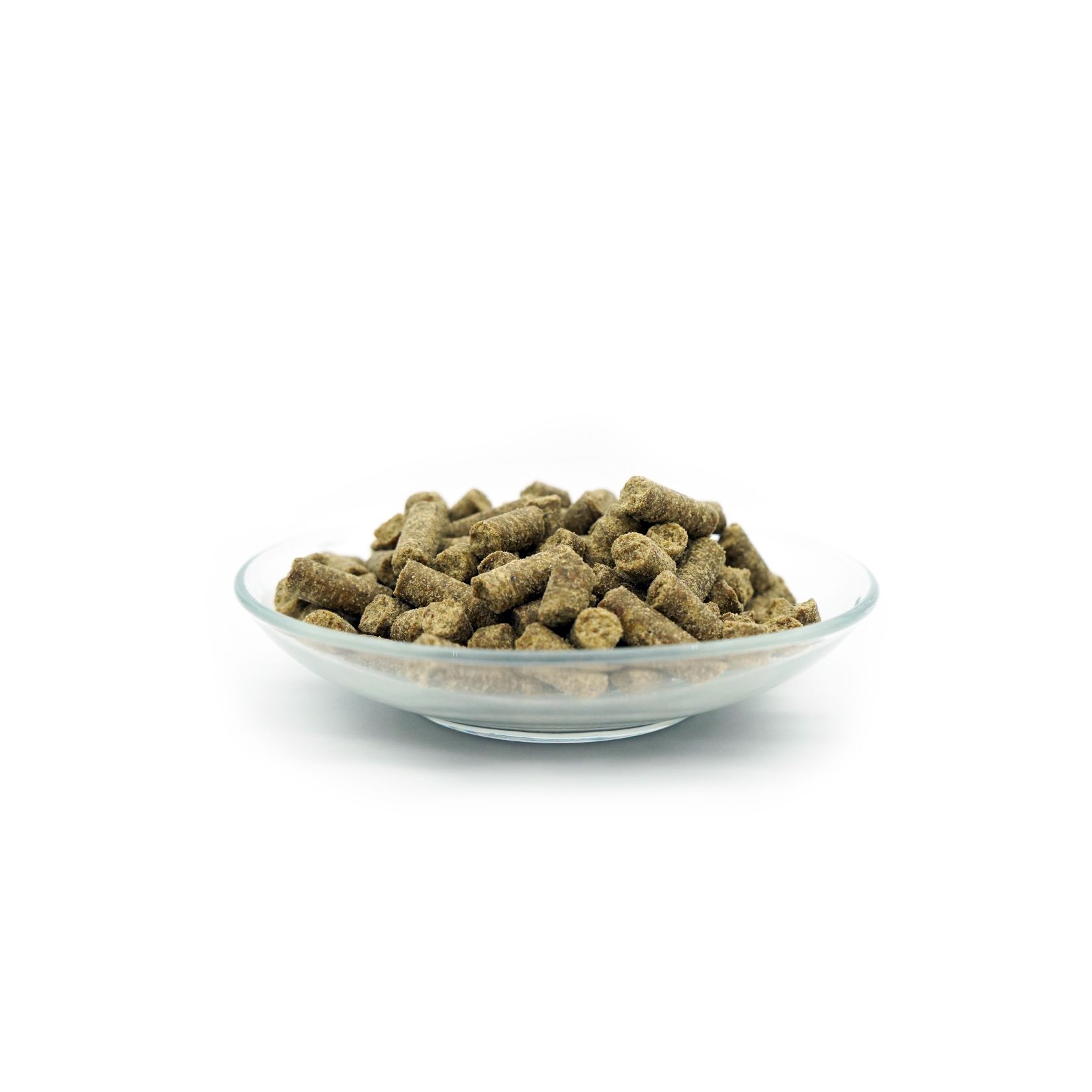 Granulés de nourriture pour chiens dans un bol en verre. Forme cylindrique verdâtre. Sur fond blanc.