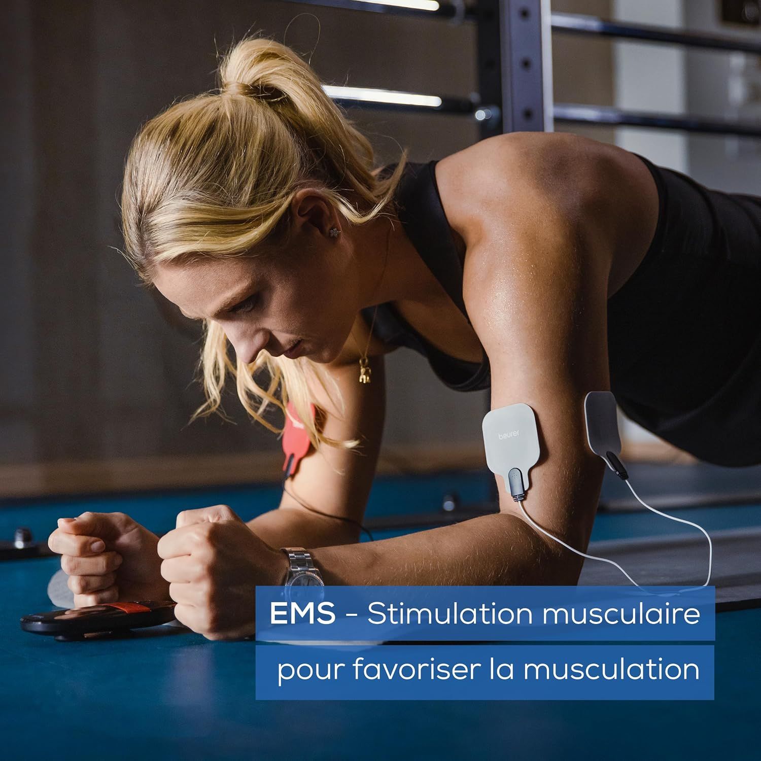 Femme en salle de sport avec électrodes EMS au bras, en position de planche.