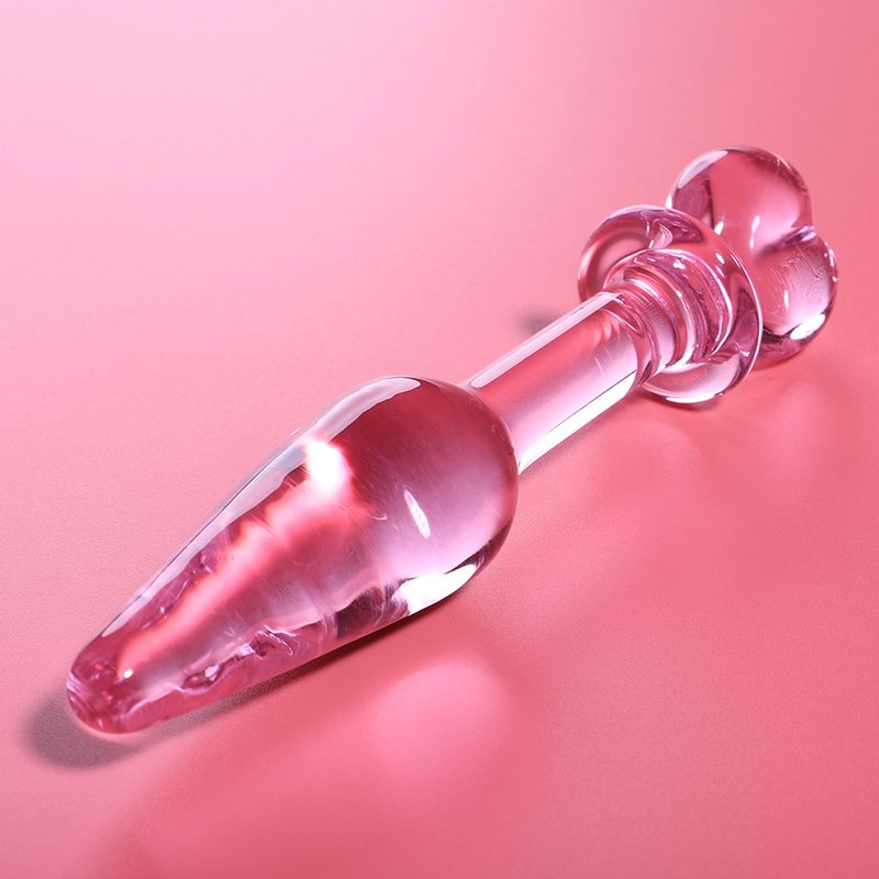 Roze glazen anale plug met hartvorm, op roze achtergrond.