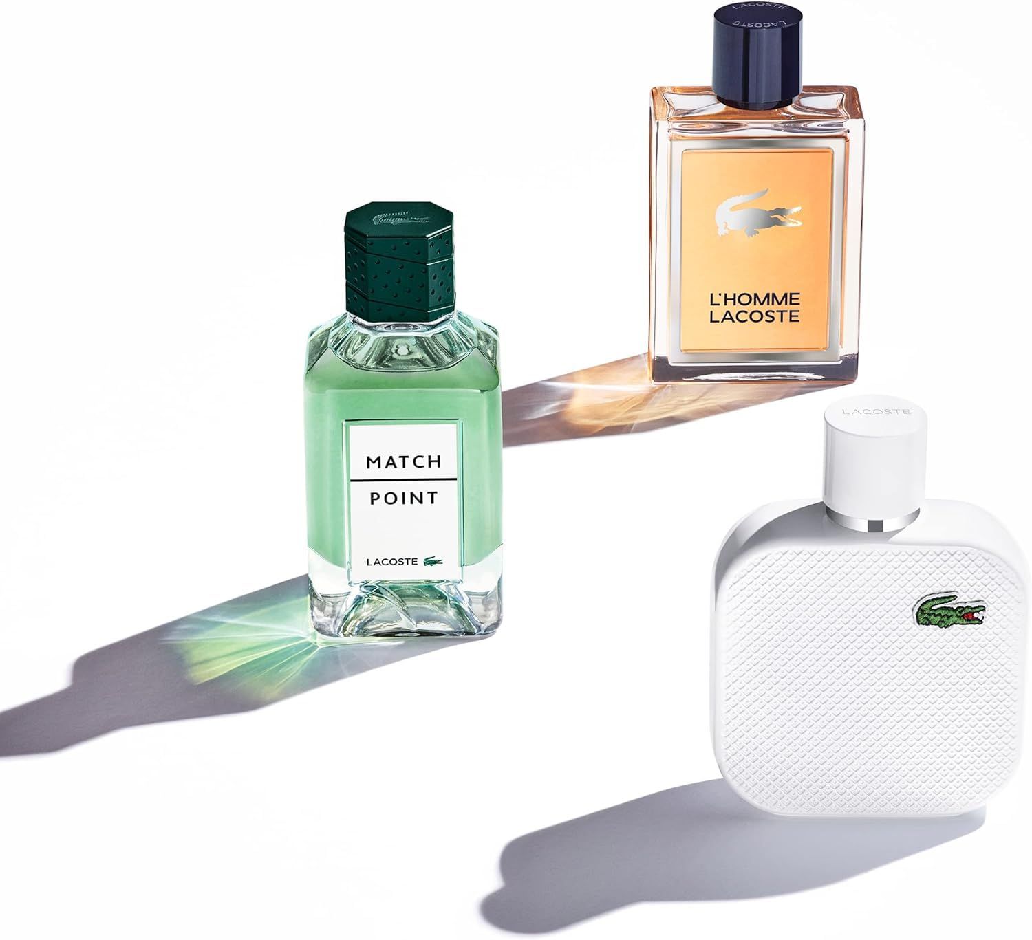 Drie Lacoste parfumflessen. L'Homme, Match Point en witte parfum. Verschillende vormen en kleuren, op witte achtergrond.
