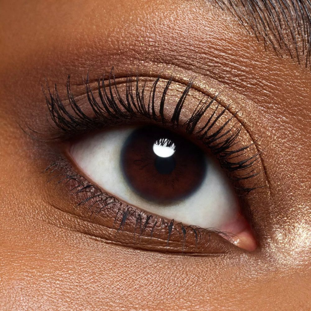 Gros plan d'un œil sur peau foncée. Les cils sont maquillés et les paupières sont maquillées.