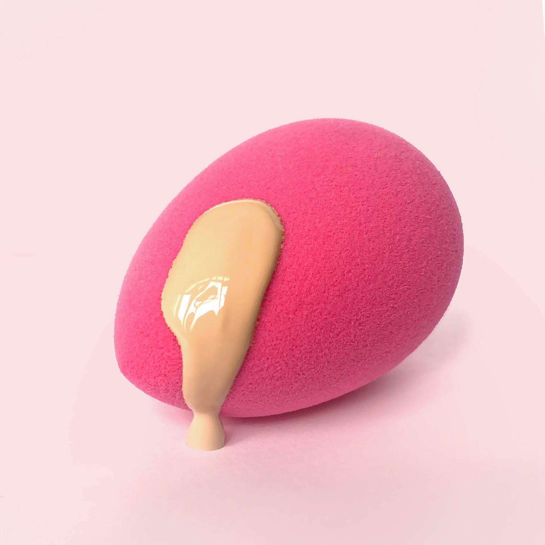 Une éponge de maquillage rose avec du fond de teint liquide qui coule.